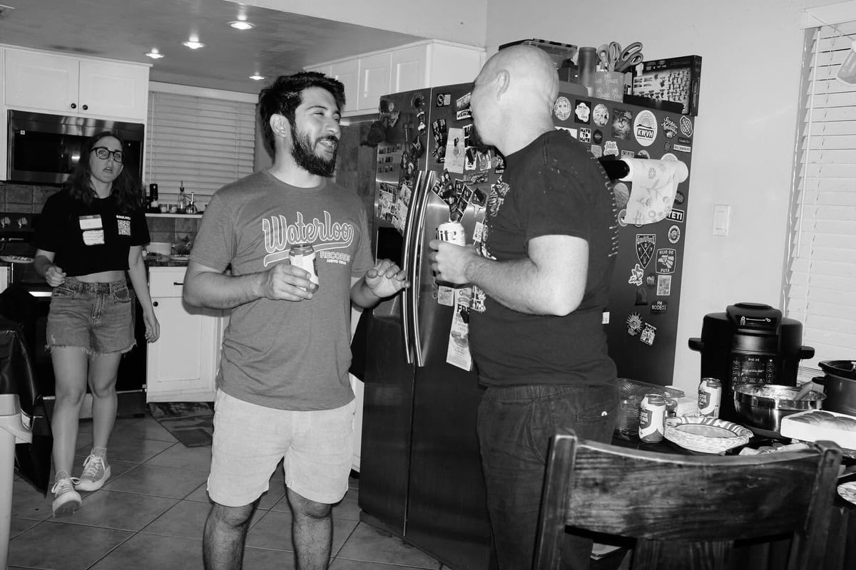 Two men conversing in a workshop with electronic equipment and tools visible in the background