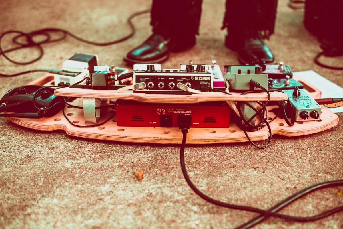 Musician with guitar pedal board setup on carpet, featuring effects processors, amplifier, and connected cables