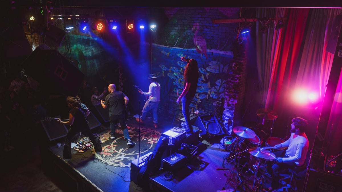 Live band performing on stage bathed in blue and magenta lighting, wide aerial stage shot