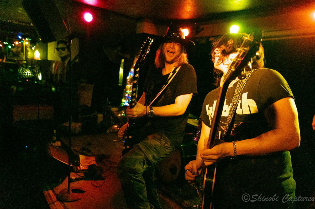Ozzy Osbourne tribute band performing on stage under colorful lighting with two guitarists and a bass player