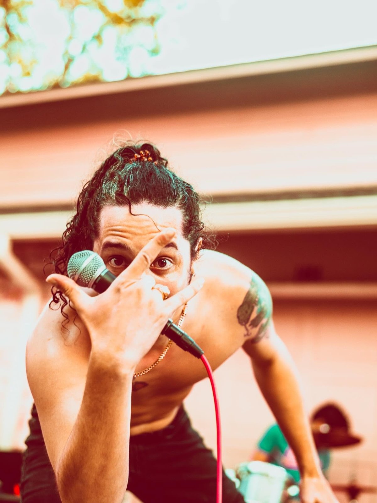 Female performer on stage holding microphone close to mouth with both hands, wearing dark top and chain necklace