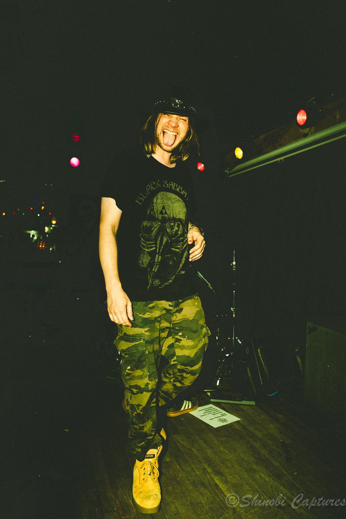 Musician in camouflage outfit performing against a dark background with glowing orbs