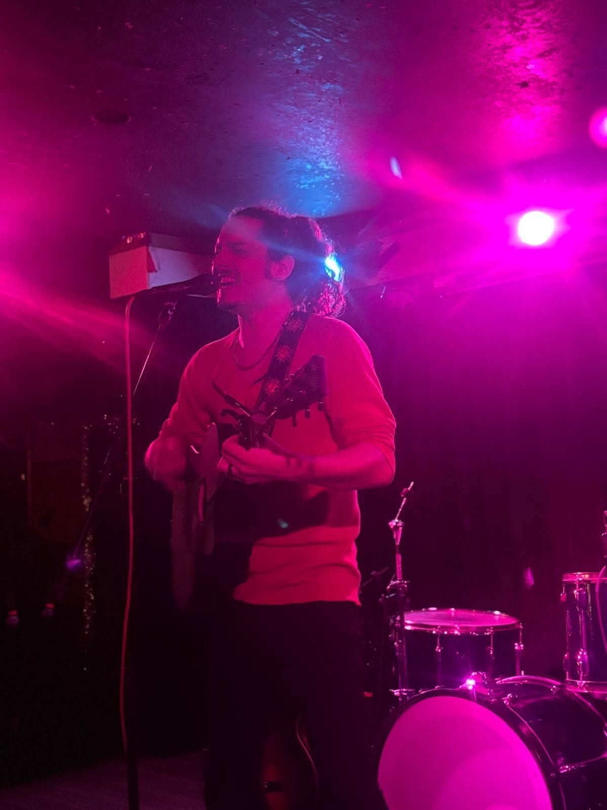 Musician performing on stage with guitar under bright pink and blue stage lighting