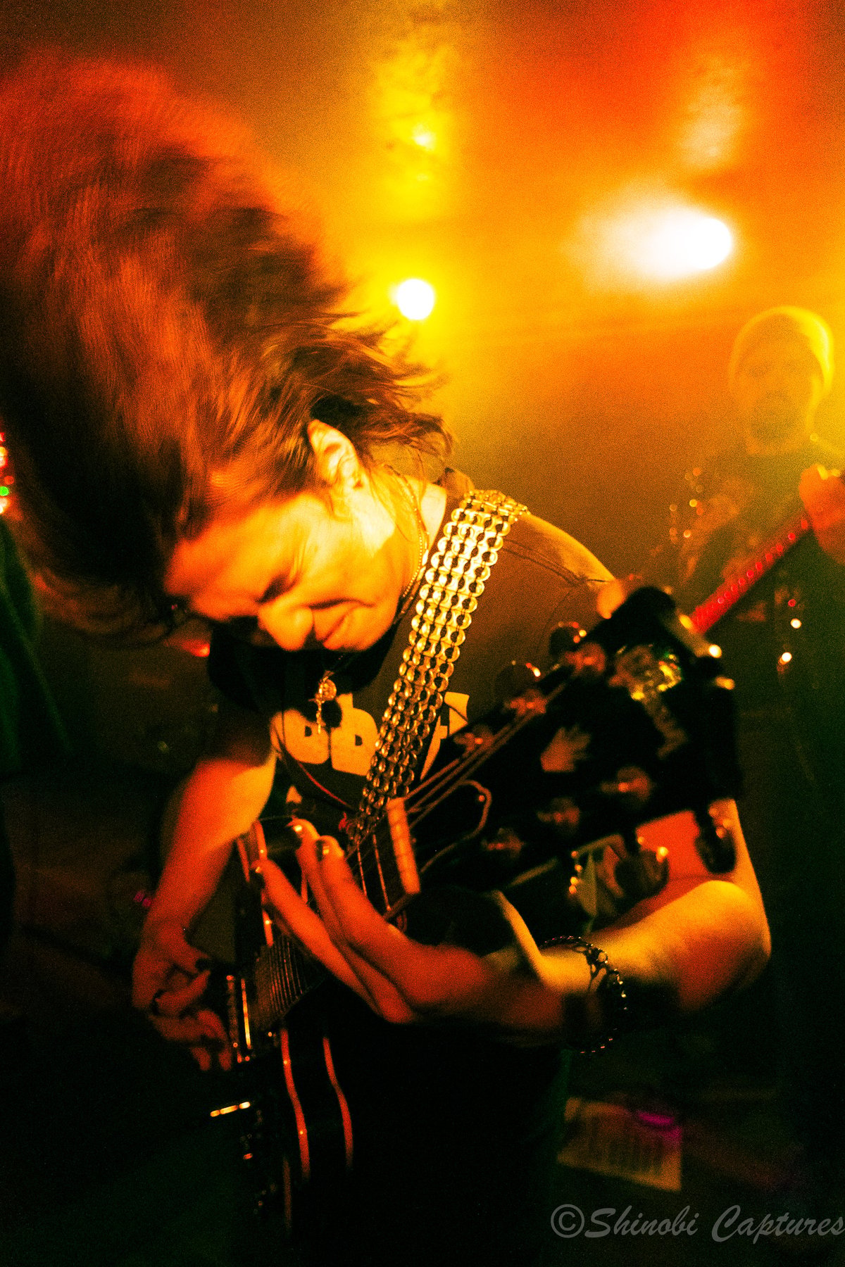 Long-haired guitarist performing under warm orange and yellow lighting during an Ozzy Osbourne tribute show