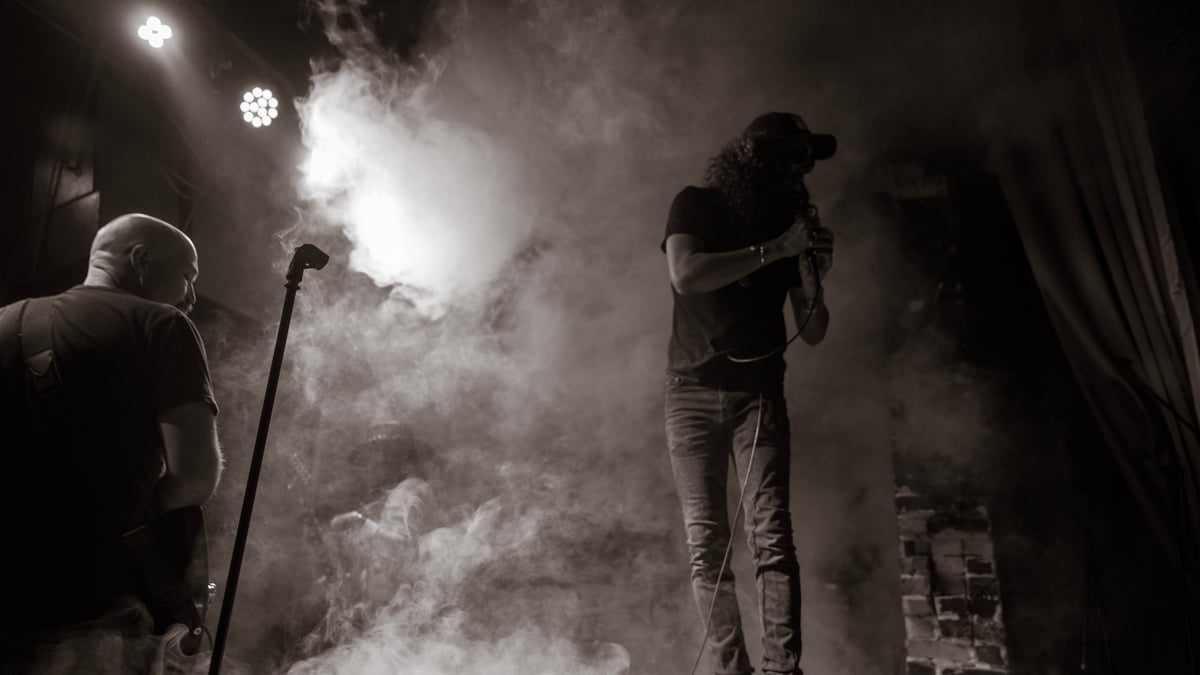 Black and white silhouette of two musicians performing amid smoke effects on stage