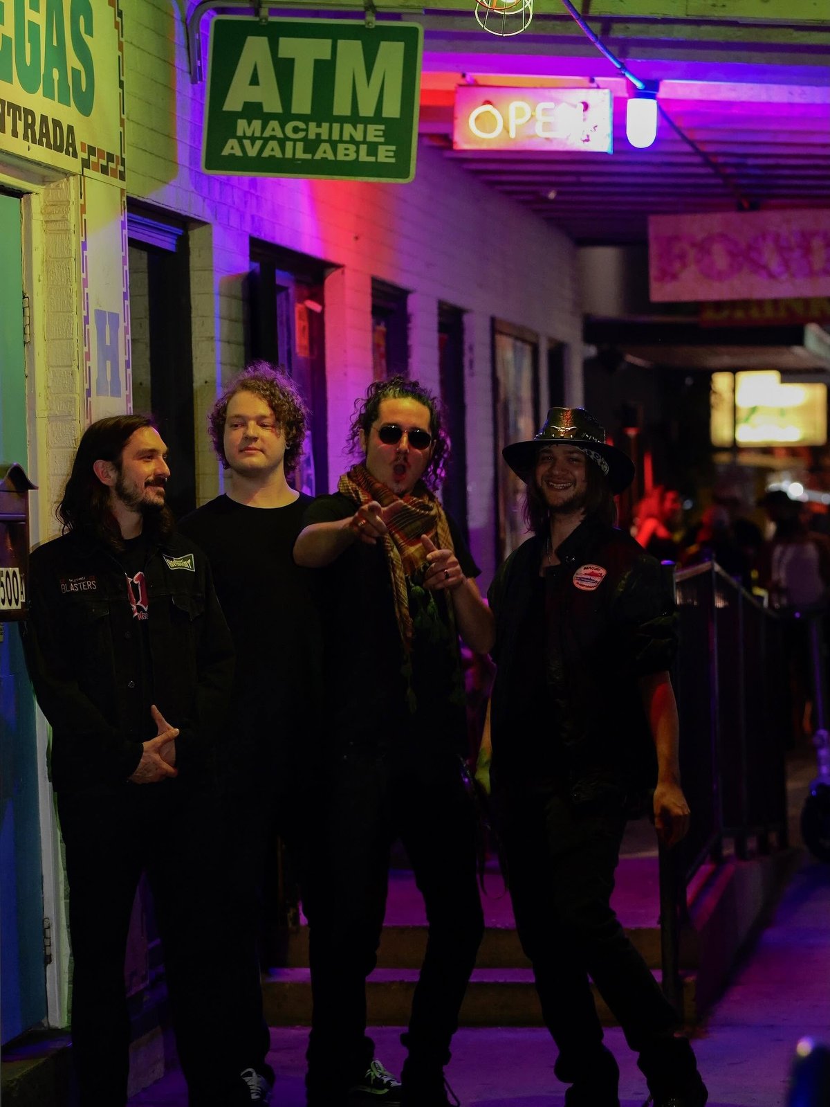 Group of four people standing in a neon-lit street at night near ATM and OPEN signs