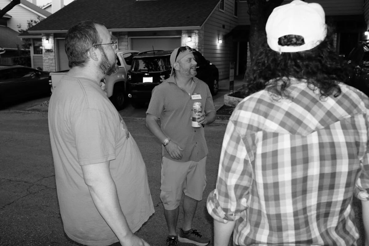 Three men standing in a parking lot at night having a conversation in black and white