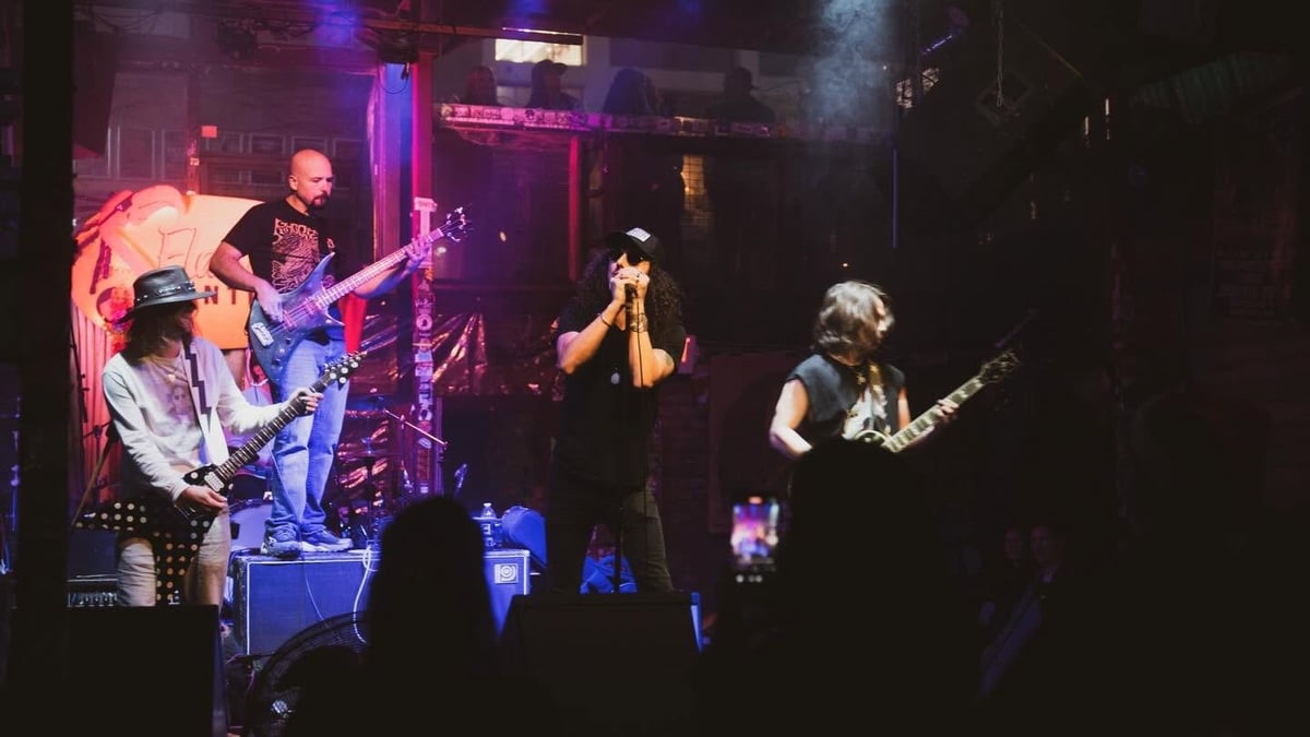 Live rock band performing on stage with guitarists, vocalist, and drummer under colorful purple and red stage lighting