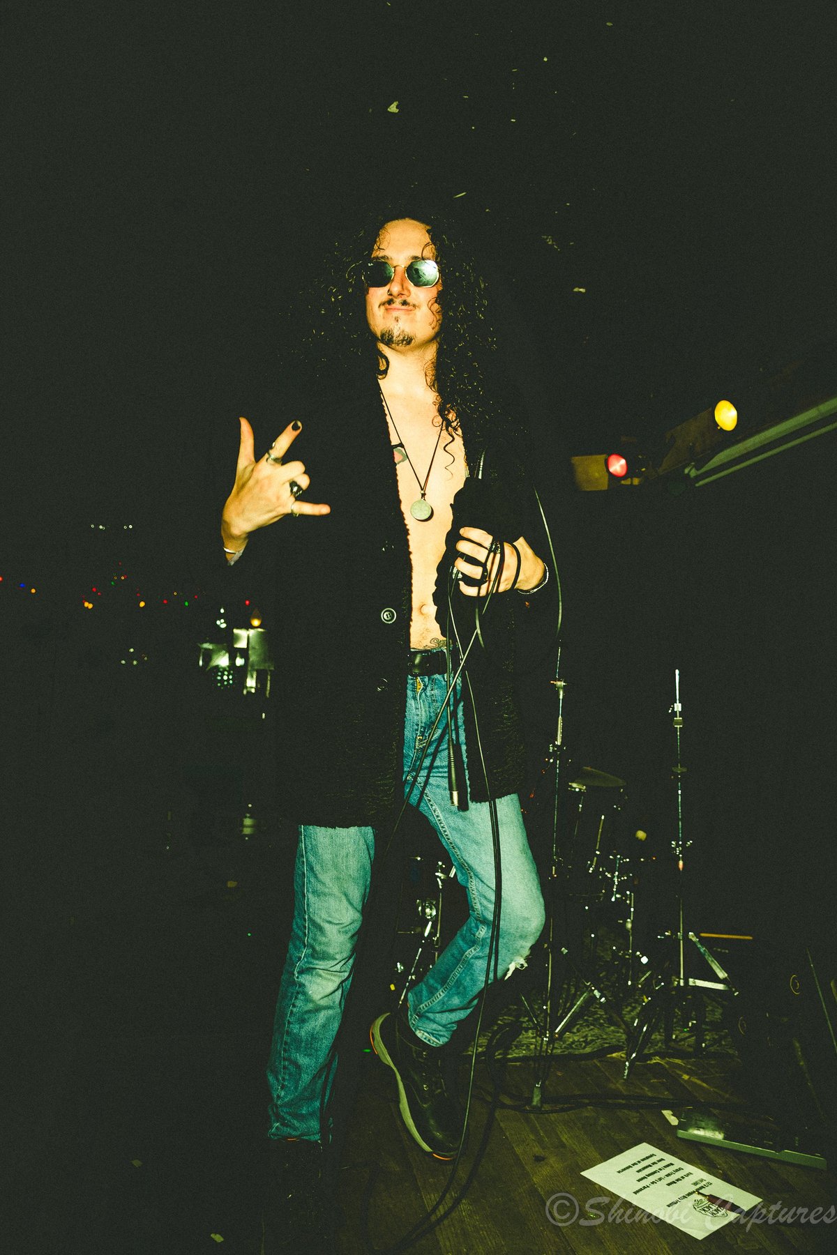 Male vocalist wearing sunglasses singing into a microphone during an Ozzy Osbourne tribute performance