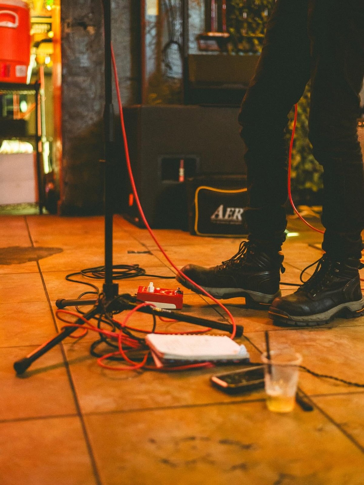 Person standing over musical equipment and cables on wooden stage floor during performance setup