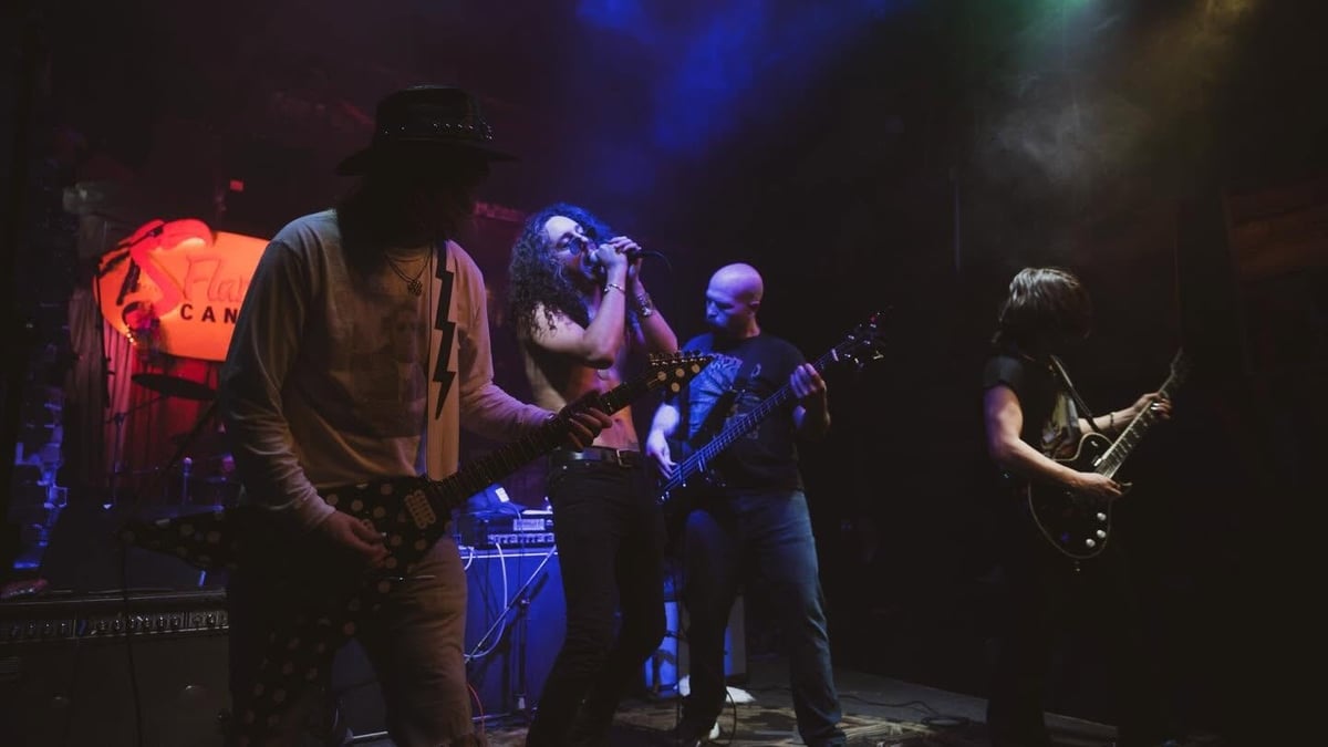 Band performing on stage with purple and red lighting, featuring vocalist, bassist, and guitarist in a live concert setting
